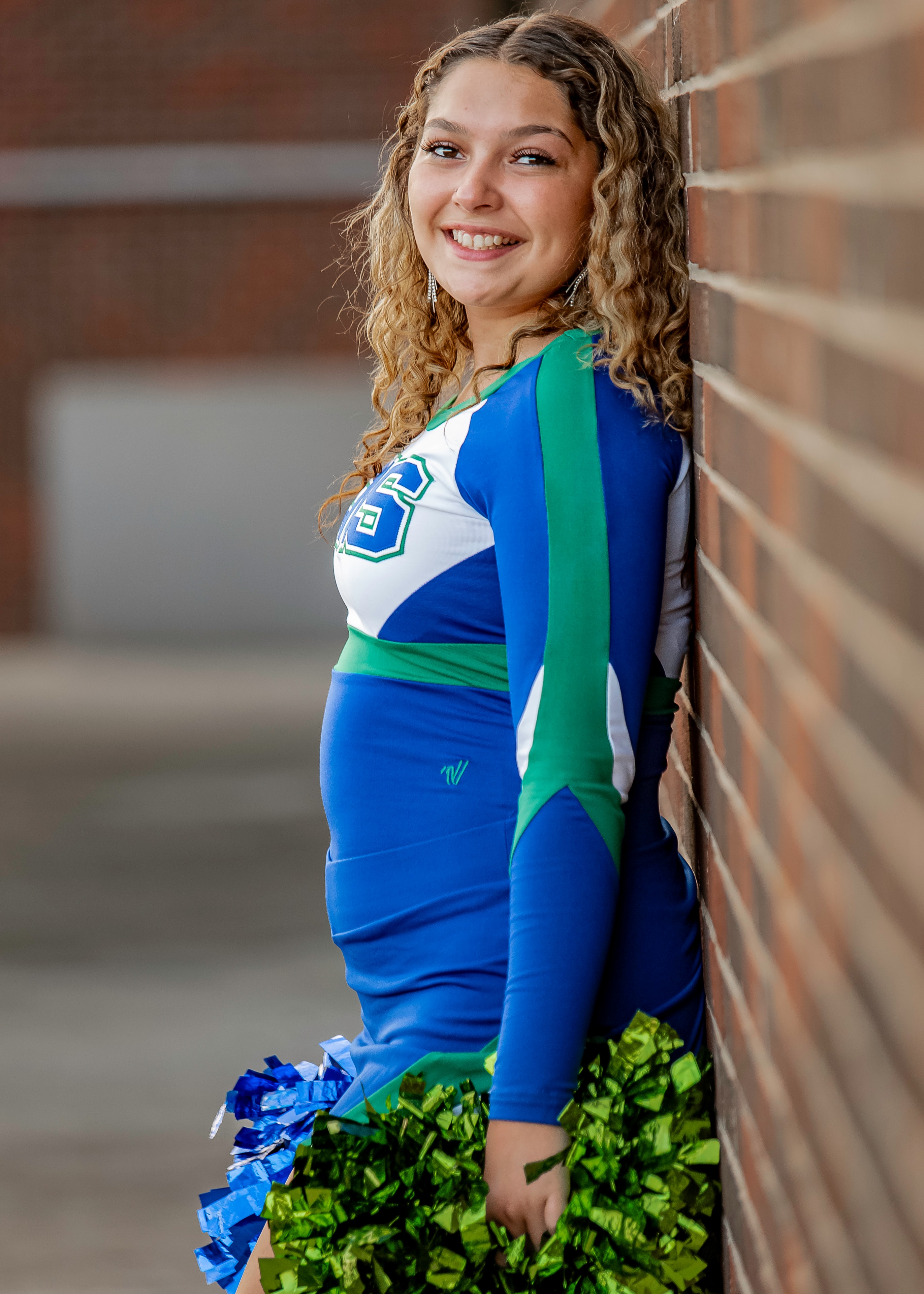 Senior cheerleader in uniform smiling against a brick wall